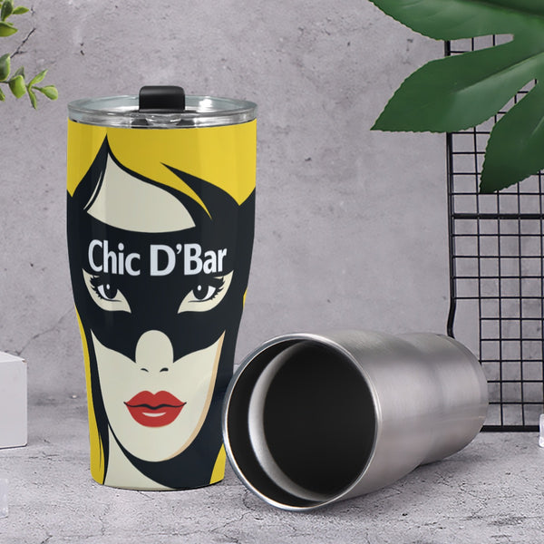 Metal tumbler with a graphic design of a face and 'Chic D'Bar' text on a gray surface.