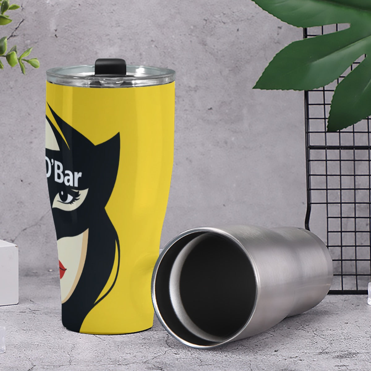 Tumbler with a graphic design on a gray surface with green leaves.