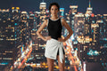 Woman in a black and white bodysuit and skirt standing in front of a city skyline at night.